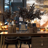 Hill Interiors Bubble Ceramic Planters in brown, displayed on a wooden dining table alongside vases, tall dark foliage stems and a gold-lettered sign.