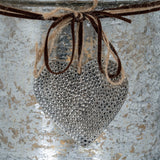 Close-up of Hill Interiors Mercury Glass Heart Large Candle Holder detail, showing a hammered silver heart charm tied with jute twine and brown suede cord.