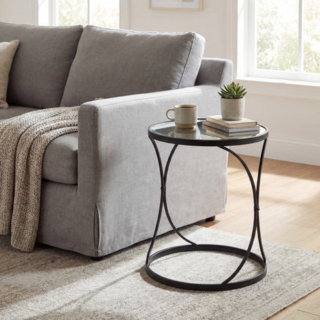 Round black side table with glass top styled with a mug, succulent and books beside a grey sofa, from Hill Interiors' Set of Two Mirrored Side Tables.