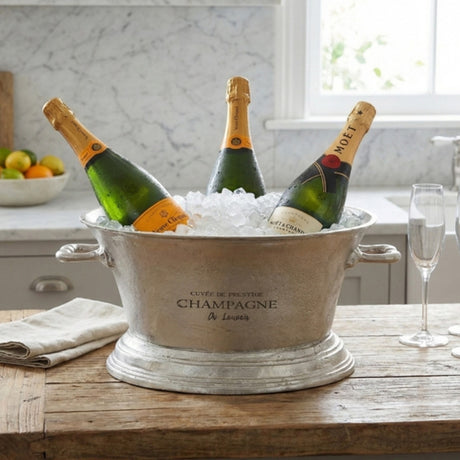 Hill Interiors Large Antique Pewter Champagne Cooler Tray in silver, holding three champagne bottles on ice, styled on a wooden kitchen counter.