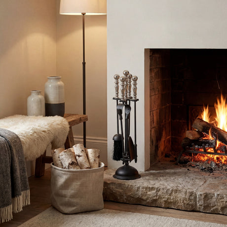Hill Interiors Chrome Handled Companion Set in silver with poker, brush, shovel and tongs on a black stand beside a lit fireplace with logs.