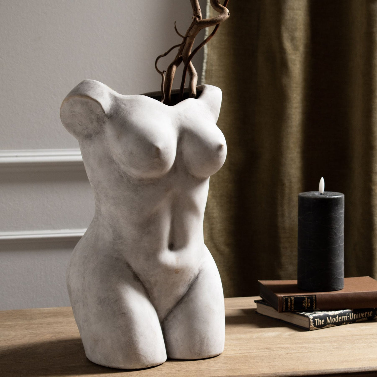 Hill Interiors beige ceramic Female Figure vase with matte sculptural torso, styled with tall twisted branches on a wooden console beside books and a candle.