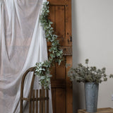 Hill Interiors Winter Garland with Lamb's Ear and Wax Flower draped along a rustic wooden door beside a linen curtain and a wooden chair.