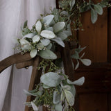 Hill Interiors Winter Garland with Lamb's Ear and Wax Flower draped over a wooden chair back, showing silvered green foliage and delicate white sprays.