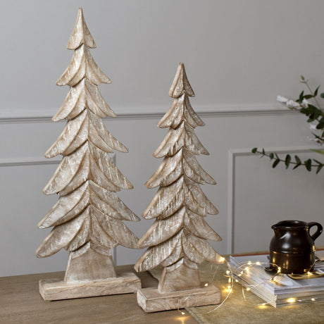 Pair of Hill Interiors Wood Christmas Tree decorations in brown, with layered fir silhouettes on square bases, styled on a table with fairy lights.