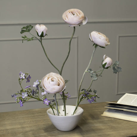 Hill Interiors ceramic flower frog vase in white with a low rounded form, holding pale pink ranunculus and purple blooms on a wooden table.