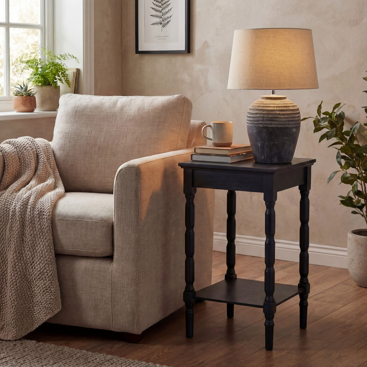 Hill Interiors Ferranock carved stone-effect ceramic table lamp in beige with tapered shade, styled on a black side table beside a linen armchair.