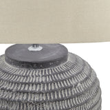 Close-up of Hill Interiors Ferranock ceramic table lamp showing carved stone-effect grey base detailing beneath a beige linen shade.