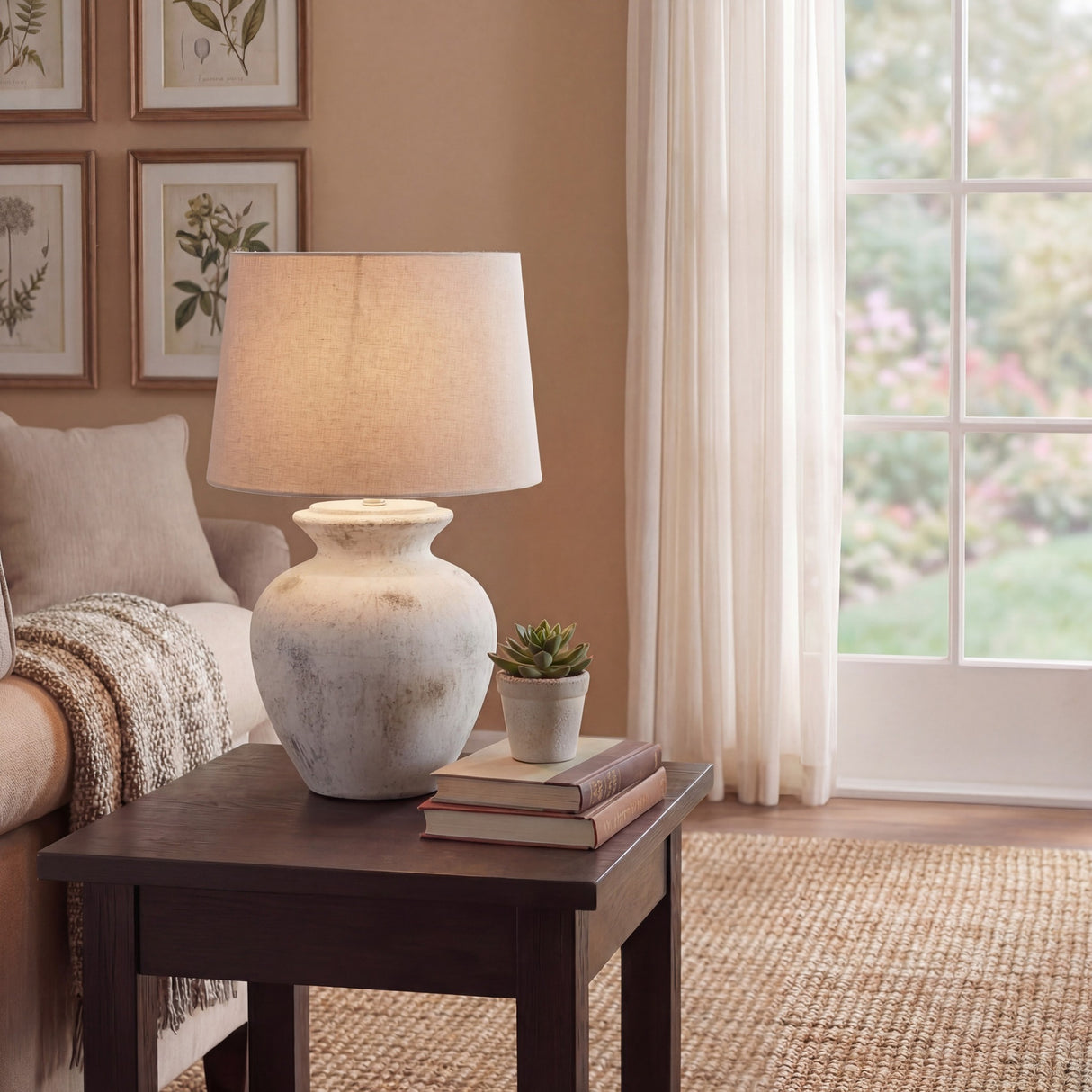 Hill Interiors ceramic table lamp with antique white glazed urn base and tapered linen shade, styled on a dark wood side table beside a sunlit window.