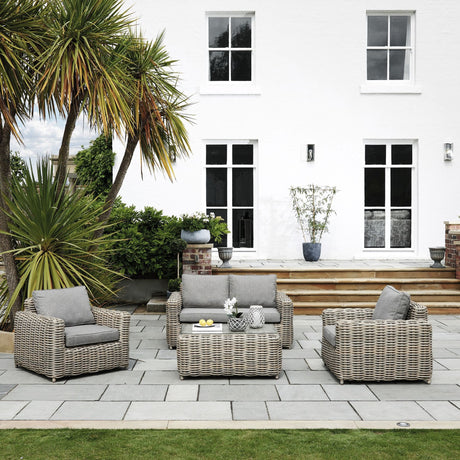 Hill Interiors four seater garden lounge set in beige woven rattan with cushioned armchairs, two-seater sofa and coffee table on a stone patio.