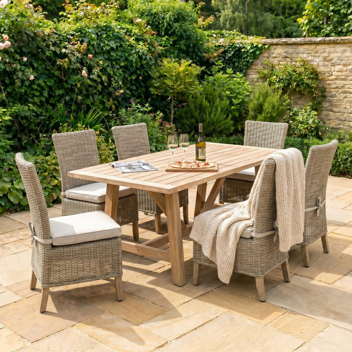 Hill Interiors beige powder-coated metal outdoor dining chairs set around a wooden garden table with wine and pizza on a sunny patio.