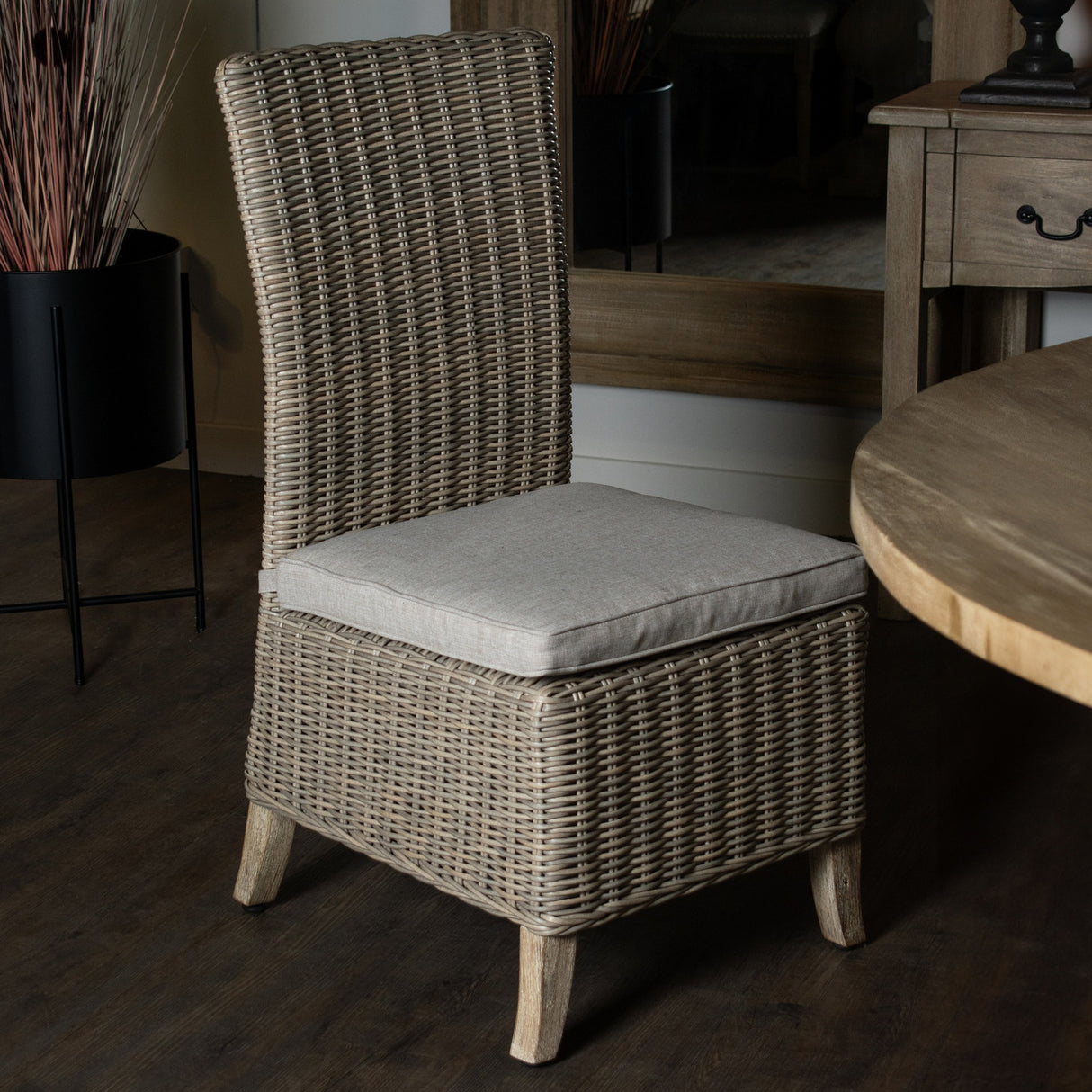 Hill Interiors woven high-back dining chair in beige with a linen seat cushion and wooden legs, placed beside a round timber table and mirror.