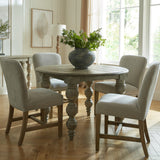 Hill Interiors Grey Wooden Dining Chairs with nailhead trim and neutral upholstery, set around a round wooden table in a sunlit dining room.