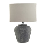 Hill Interiors Ferranock grey ceramic table lamp with rounded textured base and natural linen drum shade, shown on a plain white background.