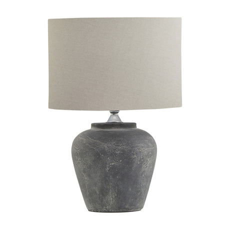 Hill Interiors Ferranock grey ceramic table lamp with rounded textured base and natural linen drum shade, shown on a plain white background.