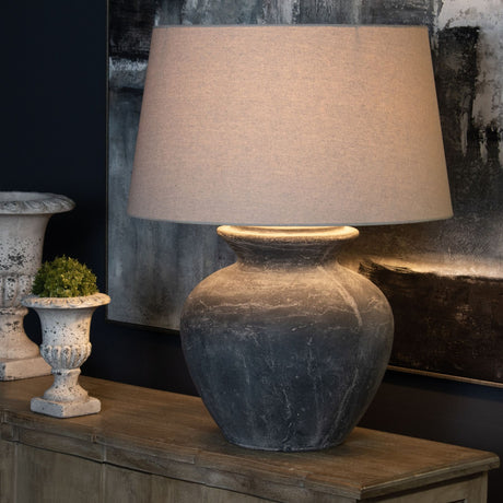 Hill Interiors Ferranock round ceramic table lamp with weathered grey base and natural linen tapered shade, styled on a wooden console with stone urn.