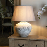 Hill Interiors Mestola large fluted ceramic table lamp in beige with a tapered linen shade, lit on a wooden sideboard beside orchids in a styled interior.