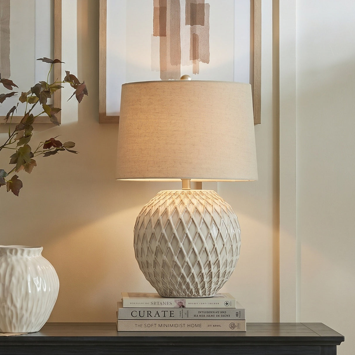Hill Interiors Lattice Ceramic Table Lamp in white with raised diamond texture and linen drum shade, styled on books beside a vase and framed prints.