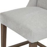Close-up of the Hill Interiors Braxdon Wooden Bar Stool in grey, showing the padded seat cushion, low upholstered back and wooden leg detail.