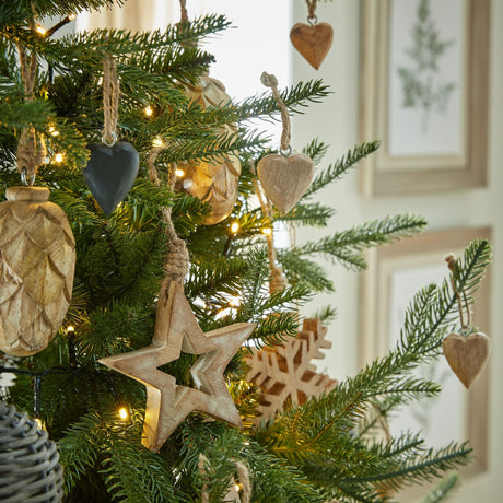 Hill Interiors wooden hanging hearts in soft brown displayed on a lit Christmas tree with pinecone, star and snowflake wood decorations.