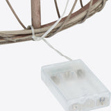 Close-up of the Hill Interiors LED wicker Christmas tree base showing woven brown branches and the clear battery pack for the LED string lights.