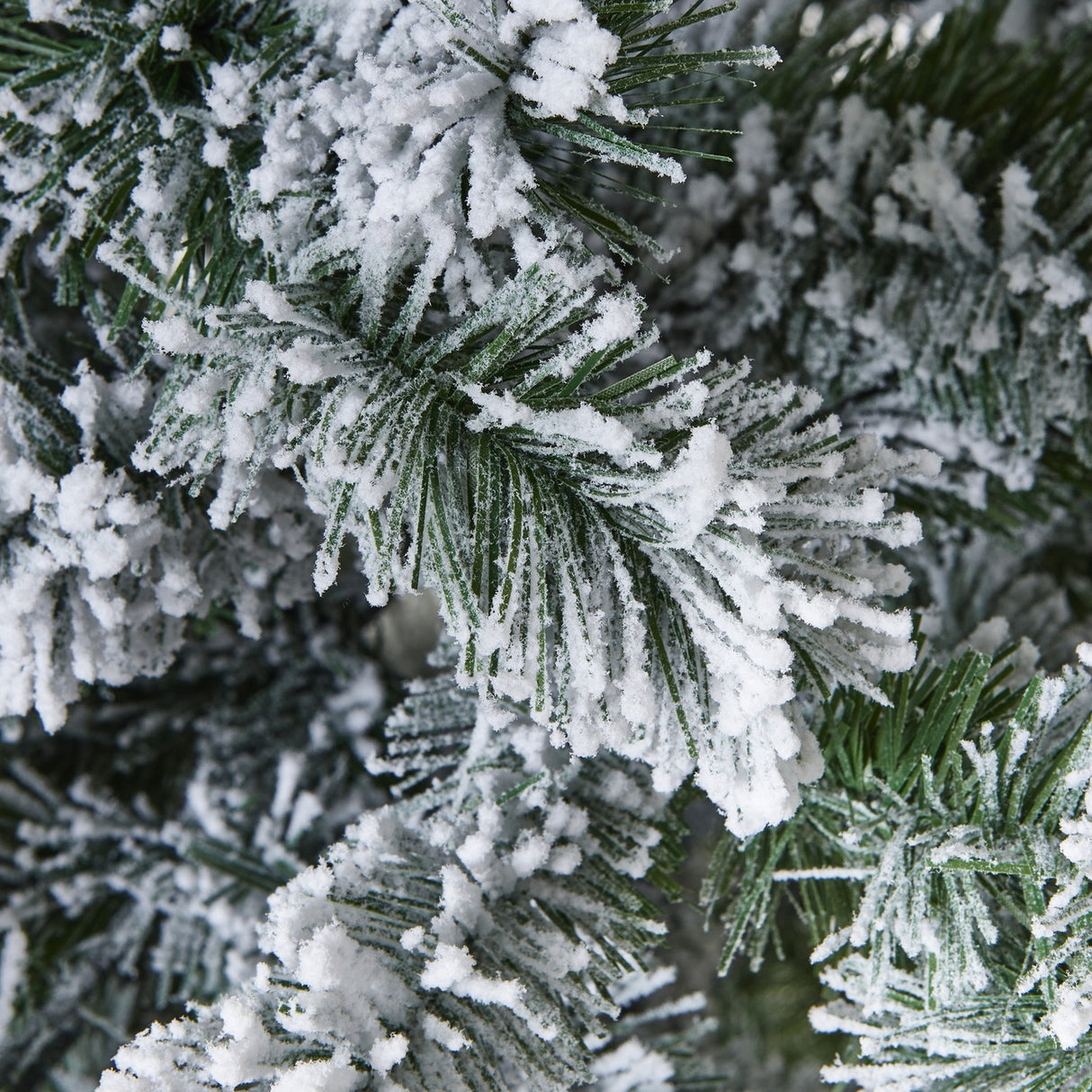 Close-up of Hill Interiors Extra Large Snowy Spruce Tree branches, showing deep green plastic needles heavily dusted with white snow-effect flocking.