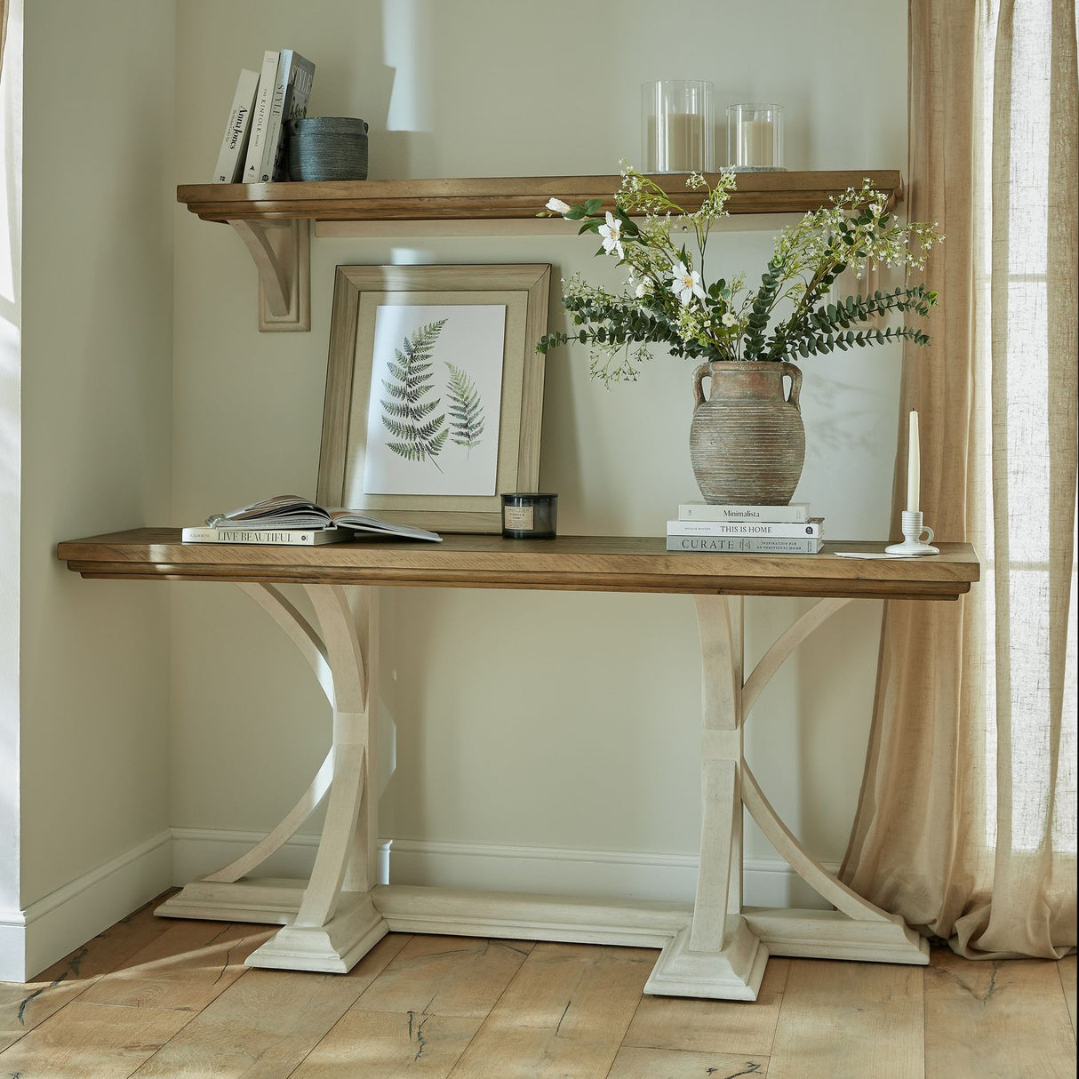 Hill Interiors brown ceramic amphora vase with tall white floral and eucalyptus stems, styled on a wooden console table beside a fern print and books.