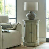 Hill Interiors Lumbriden Lekanis ceramic table lamp with brown urn-shaped base and drum shade on a round wooden cabinet in a bright living room.