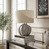 Hill Interiors Merenza fluted ceramic table lamp in antique white with a drum shade, styled on stacked books atop a glass console table.
