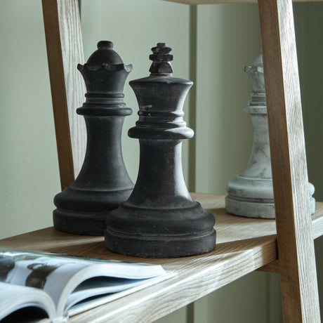 Hill Interiors Grey Queen Chess Piece styled on a wooden shelf beside a dark king and queen, with an open book below.