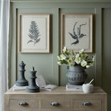 Hill Interiors Grey Queen and King ceramic chess pieces styled on a wood console with books, a patterned vase of white blooms and framed fern prints.