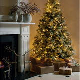 Hill Interiors Grey Stone Effect Penguin Statues in beige ceramic displayed on a white mantel with berry stems, beside a lit Christmas tree and gifts.