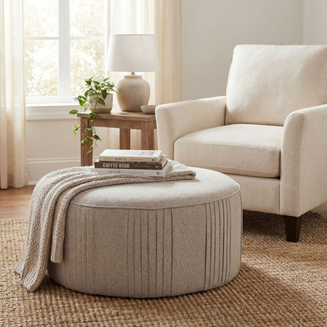 Hill Interiors Swivel Ottoman in oatmeal twill with pleated detailing, styled with books and a knit throw beside a cream armchair on a jute rug.