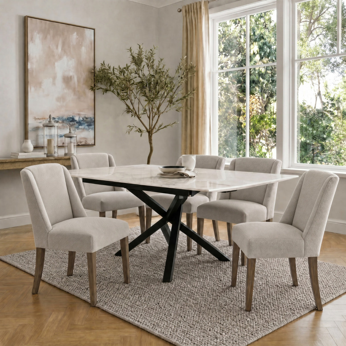 Hill Interiors Braxdon Aspen dining set with wooden chairs in cream upholstery around a marble-top table on textured rug in a bright dining room.