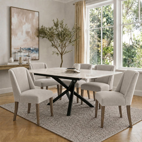 Hill Interiors Braxdon Aspen dining set with wooden chairs in cream upholstery around a marble-top table on textured rug in a bright dining room.