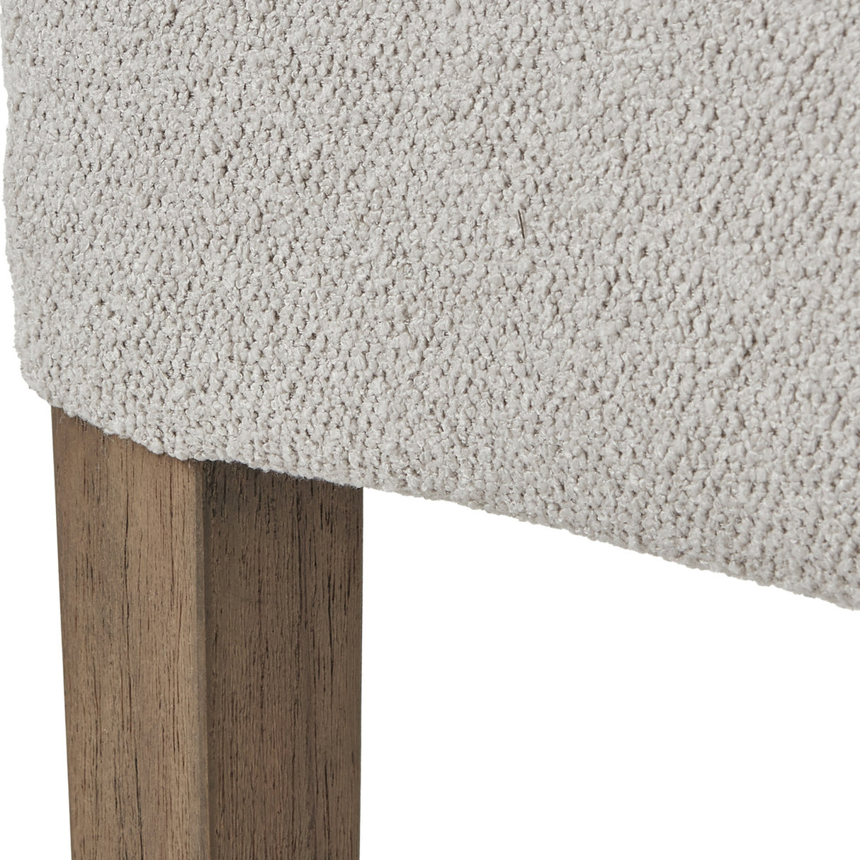 Close-up of the Hill Interiors Braxdon Aspen dining chair showing textured light grey bouclé upholstery meeting a solid wood leg with natural grain finish.