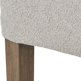 Close-up of the Hill Interiors Braxdon Aspen dining chair showing textured light grey bouclé upholstery meeting a solid wood leg with natural grain finish.