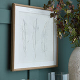 Hill Interiors White Feathers wall art with three delicate feather prints in a white beaded wooden frame, hung on a teal panelled wall beside foliage.