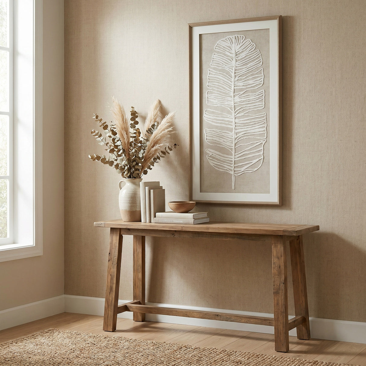 Hill Interiors Large Feather Wall Art in a beaded frame hangs above a wooden console table with a vase of pampas and eucalyptus in a neutral hallway.