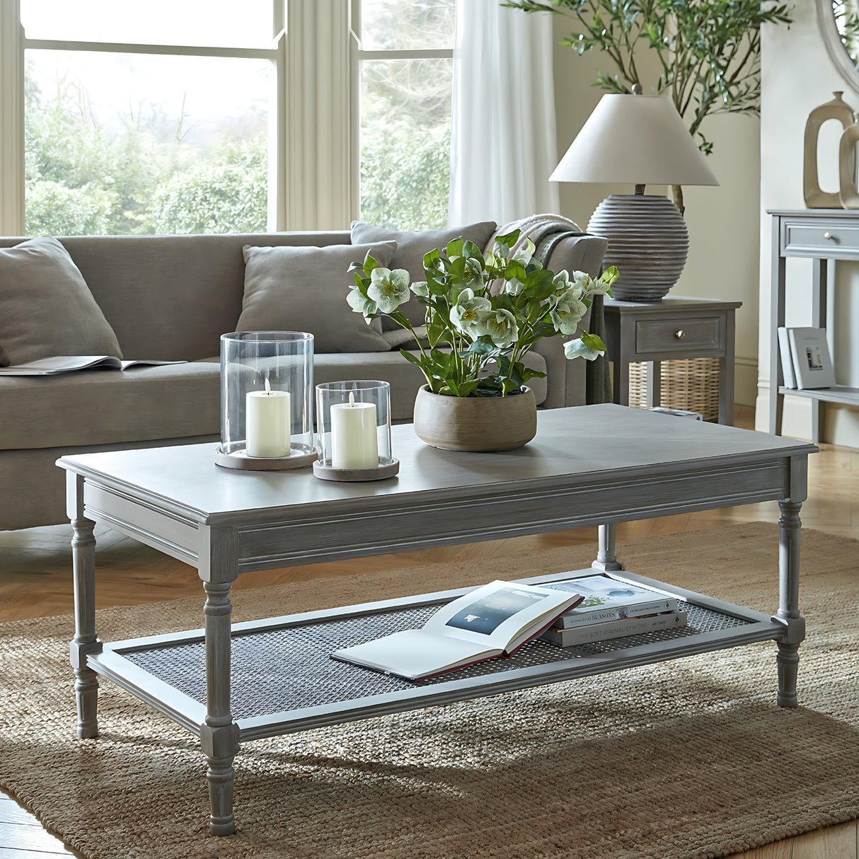 Hill Interiors Rattan Coffee Table in brown with woven lower shelf, styled with candles and hellebores in a grey living room setting.