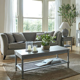 Hill Interiors Rattan Coffee Table in brown with woven lower shelf, styled with candles and flowers in a bright living room with grey sofa.