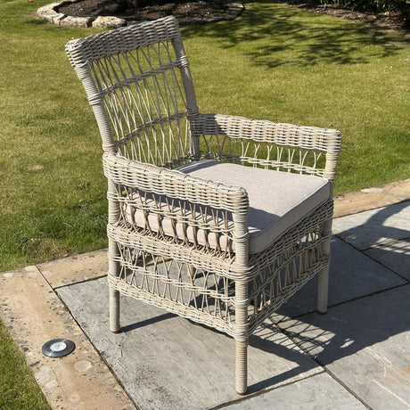 Hill Interiors beige metal outdoor dining chair with woven rattan-effect frame and cushioned seat, set on a garden patio beside a lawn.
