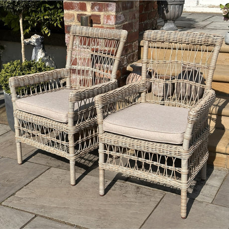 Hill Interiors beige woven outdoor dining chairs with metal frames and cushioned seats, arranged on a stone patio beside a brick wall and planters.