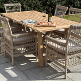 Hill Interiors beige metal outdoor dining chairs with open woven backs and cushioned seats arranged around a wooden garden table set with pizza and wine.