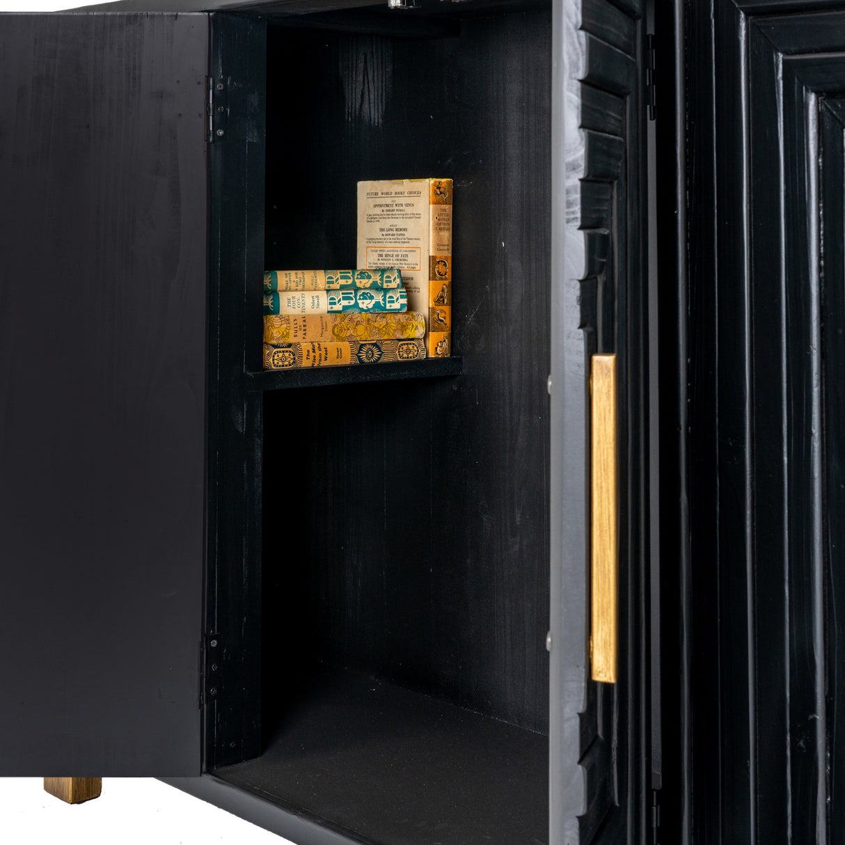 Close-up of the Hill Interiors Harweld 2-Door Sideboard in black, one door open to reveal an internal shelf with stacked books and a brushed gold handle.