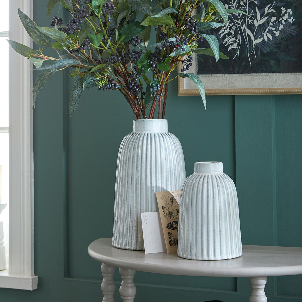 Hill Interiors Large Ceramic Bell Vase in white with ribbed body, holding tall berry and foliage stems on a console table against a green wall.