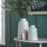 Hill Interiors Medium Bell Vase in white ribbed ceramic paired with a taller vase on a console table, holding foliage with dark berries against a green wall.