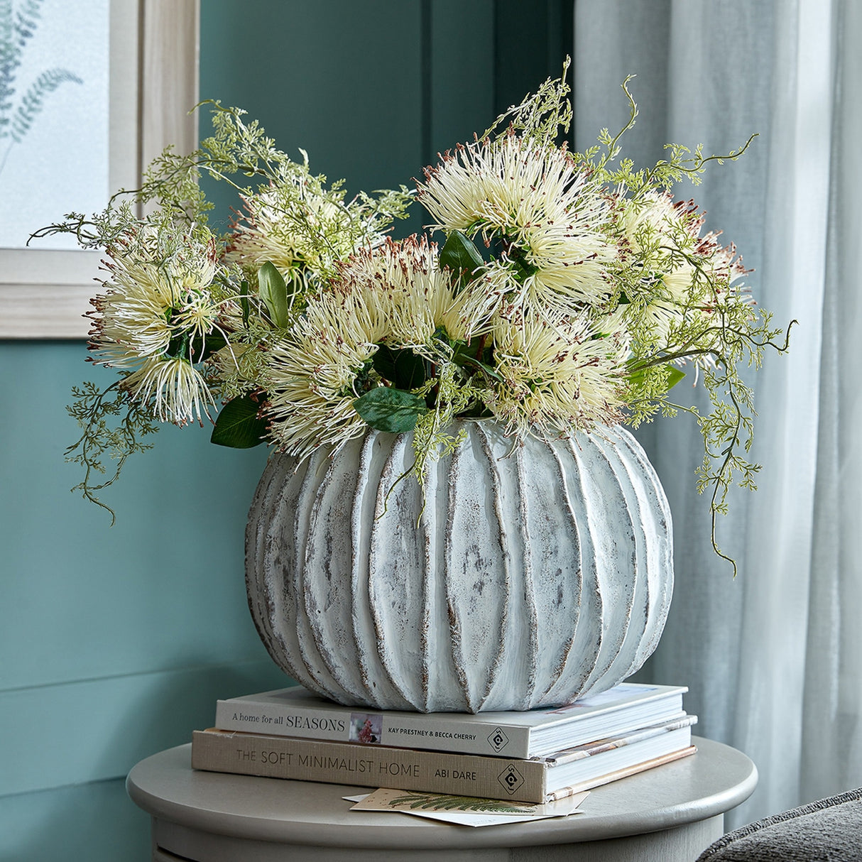 Hill Interiors Rounded Ceramic Fin Vase in white with ridged body, holding cream bloom arrangement on stacked books atop a side table.