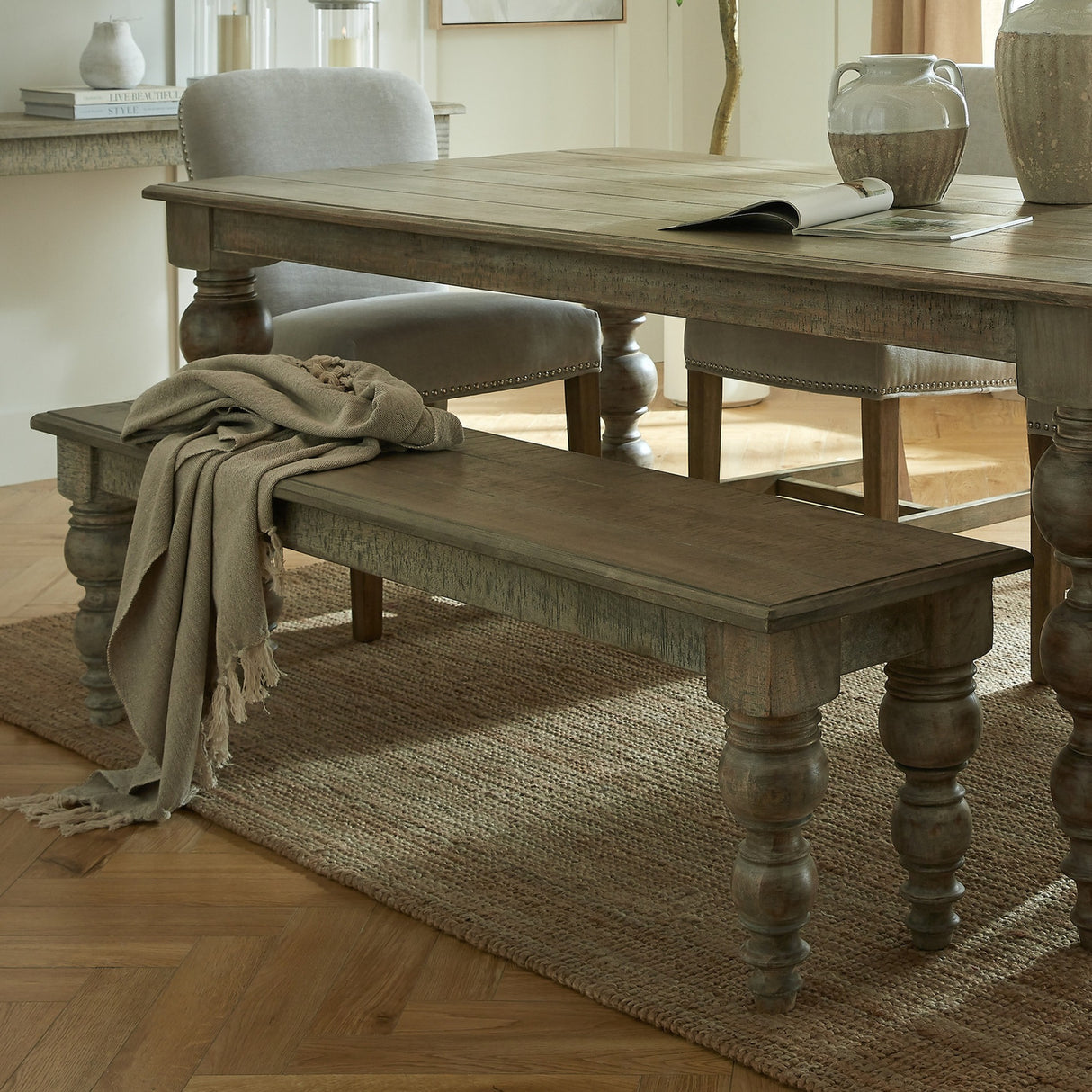 Hill Interiors Rectangular Wooden Bench in brown with turned legs, styled beneath a dining table on a jute rug with a draped linen throw.