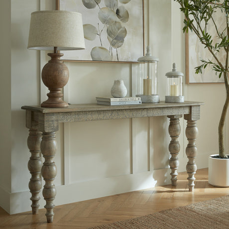 Hill Interiors Wooden Console Table in brown with turned bobbin legs, styled in a hallway with a lamp, lanterns and framed botanical art.